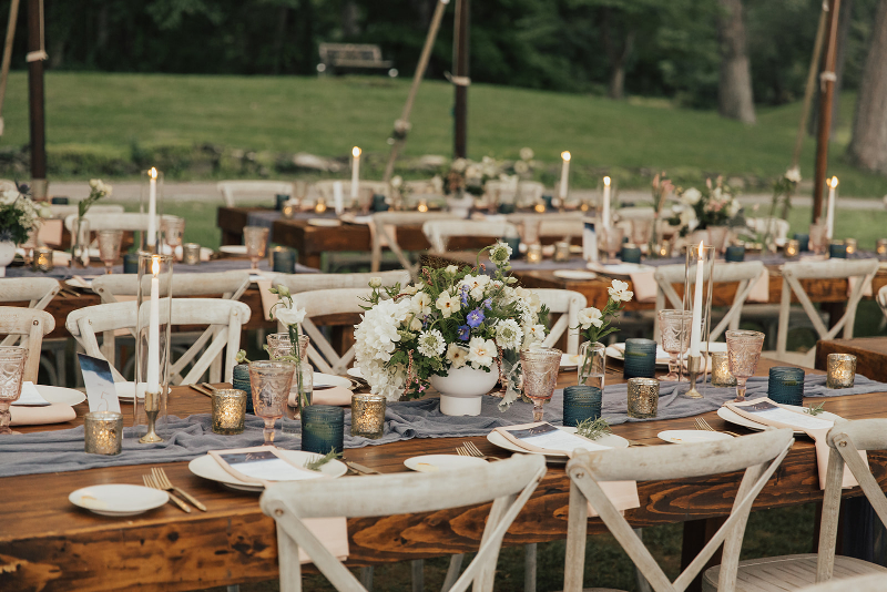 closeup of wedding table decorated with light blue table runners, white and greenery centerpieces, and rustic wedding decor