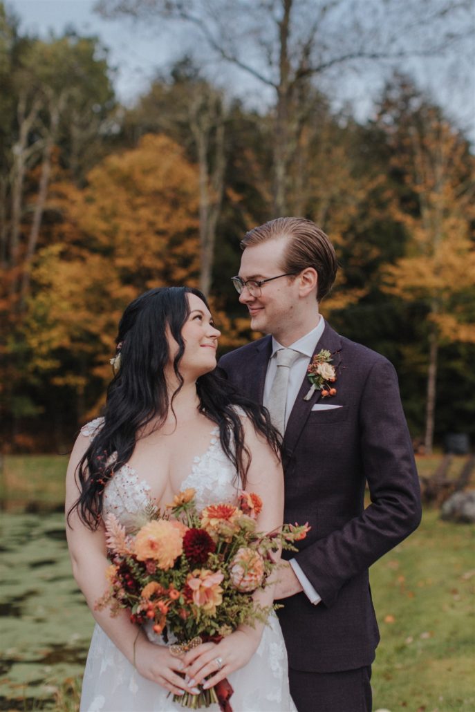 Emily and Greg taking romantic photos on the lush, scenic grounds of Antrim Streamside, surrounded by vibrant fall foliage.