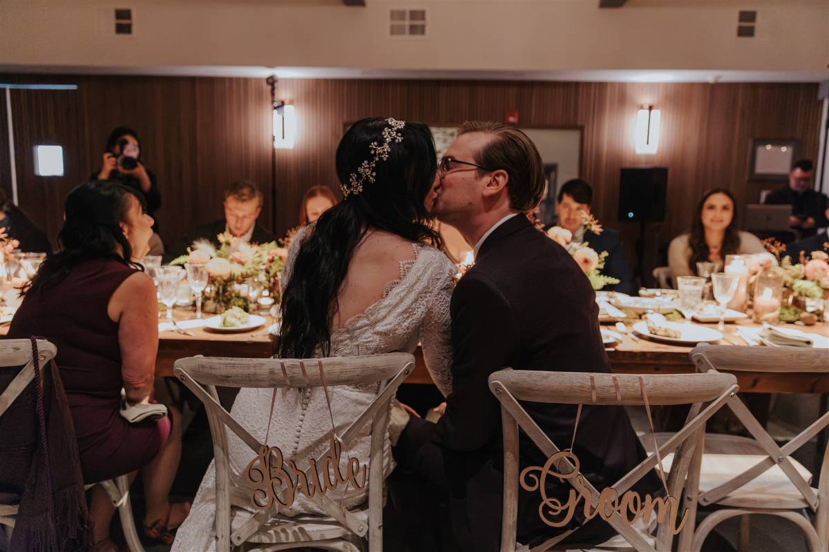 the couple sharing an intimate kiss in view is their "Bride" & "Groom" seat signs.
