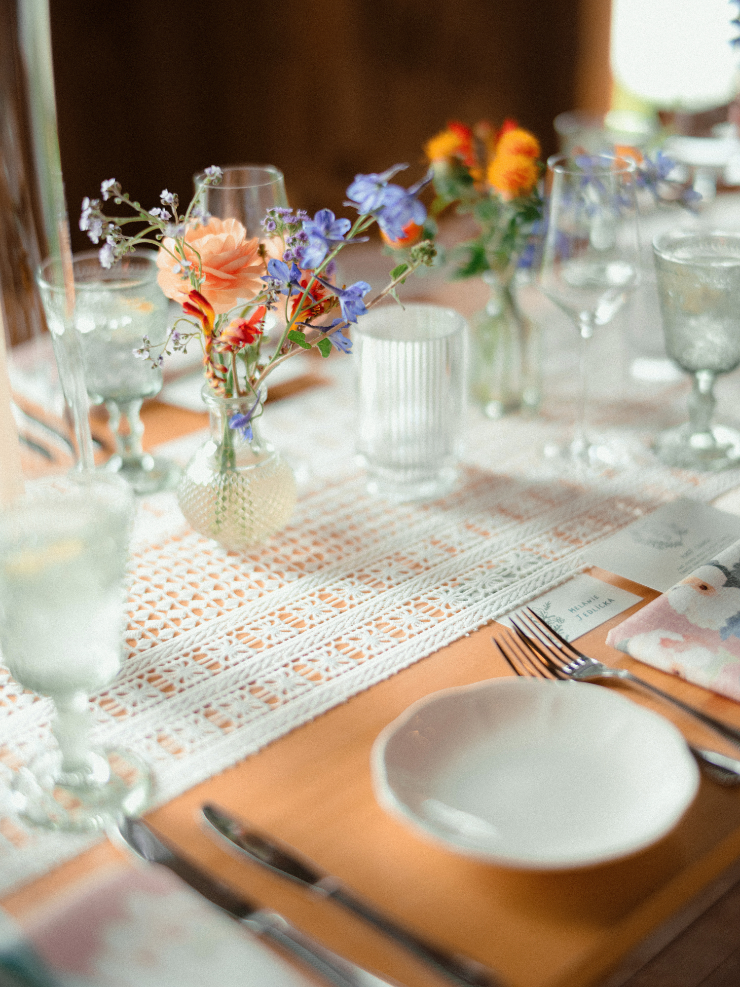 close up shot of wedding reception tablescape details. featuring white plates, and peach, purple, and burgundy blooms placed on white textured table runner