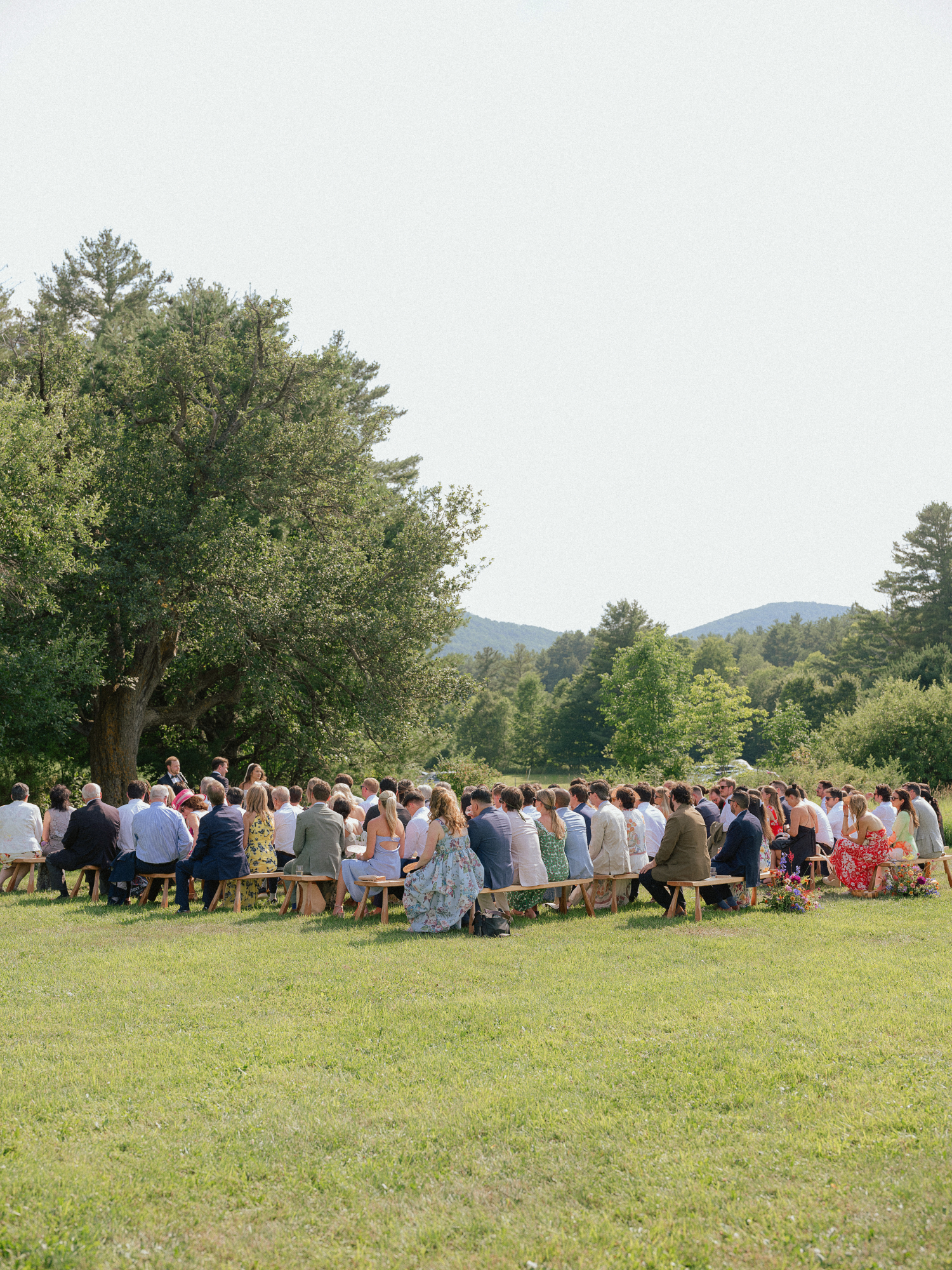 barn wedding guests sitting on wooden benches in an outdoor setting