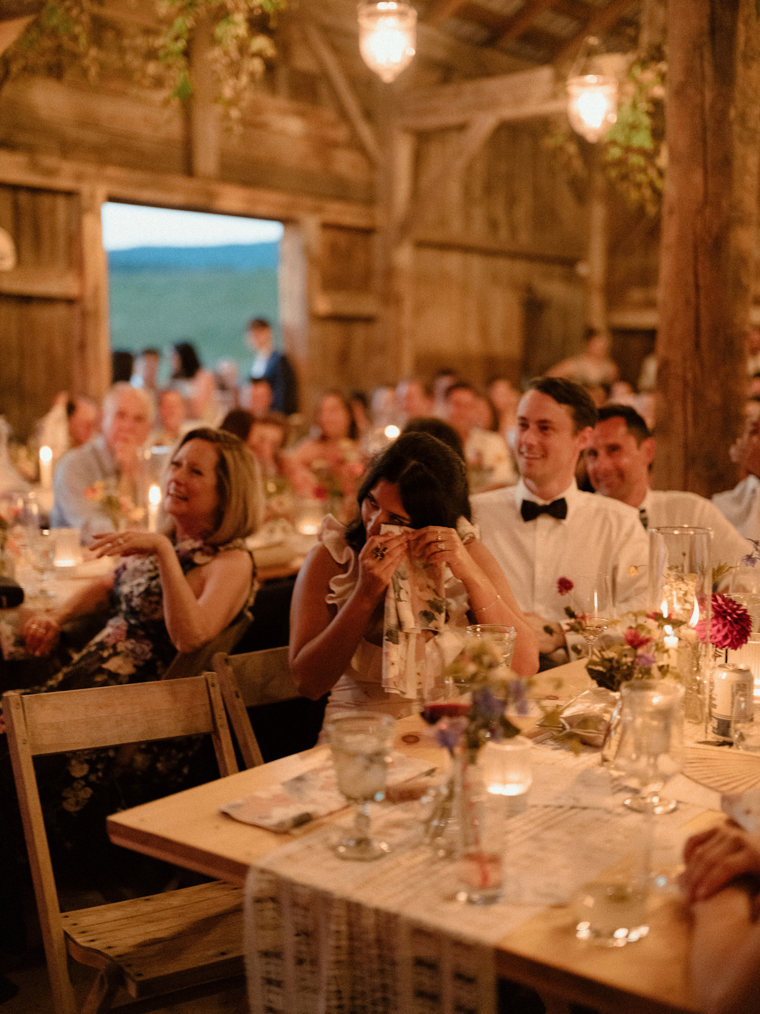 centered on a guest wiping away tears during wedding reception speeches and other guests listening at speaker