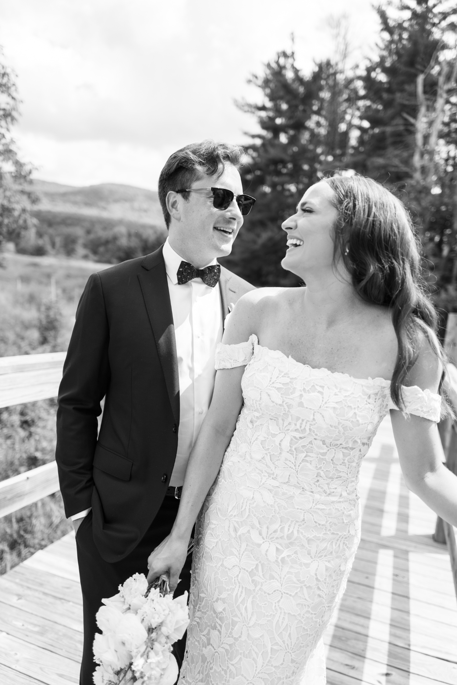 black and white shot of bride and groom outside barn wedding smiling at each other - bride is holding her white floral bouquet