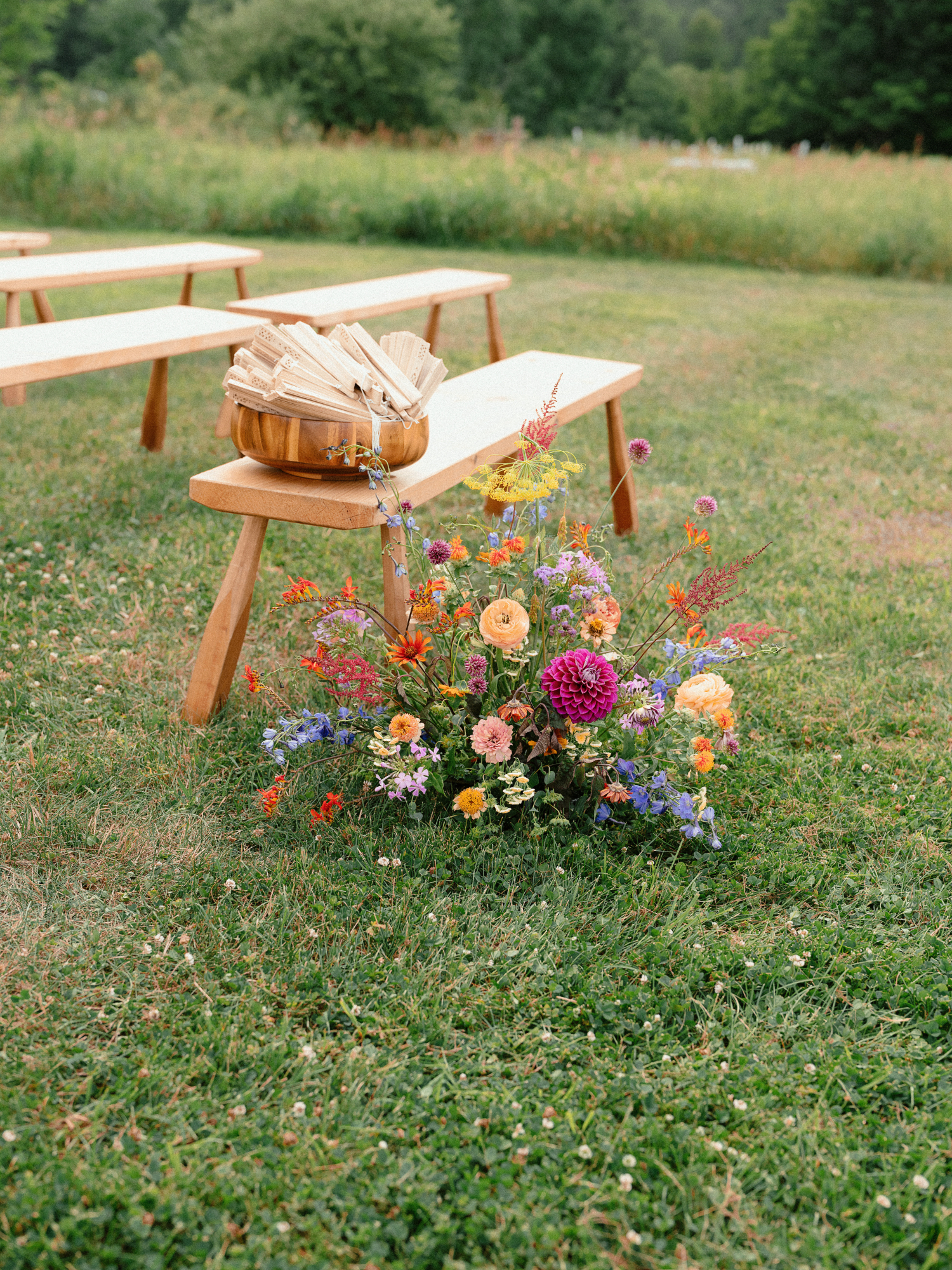  A vibrant mix of pink dahlias, orange ranunculus, blue blooms, and wildflowers adds a pop of color next to wooden ceremony benches