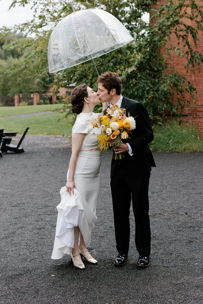 bride and groom kiss in the rain under umbrella