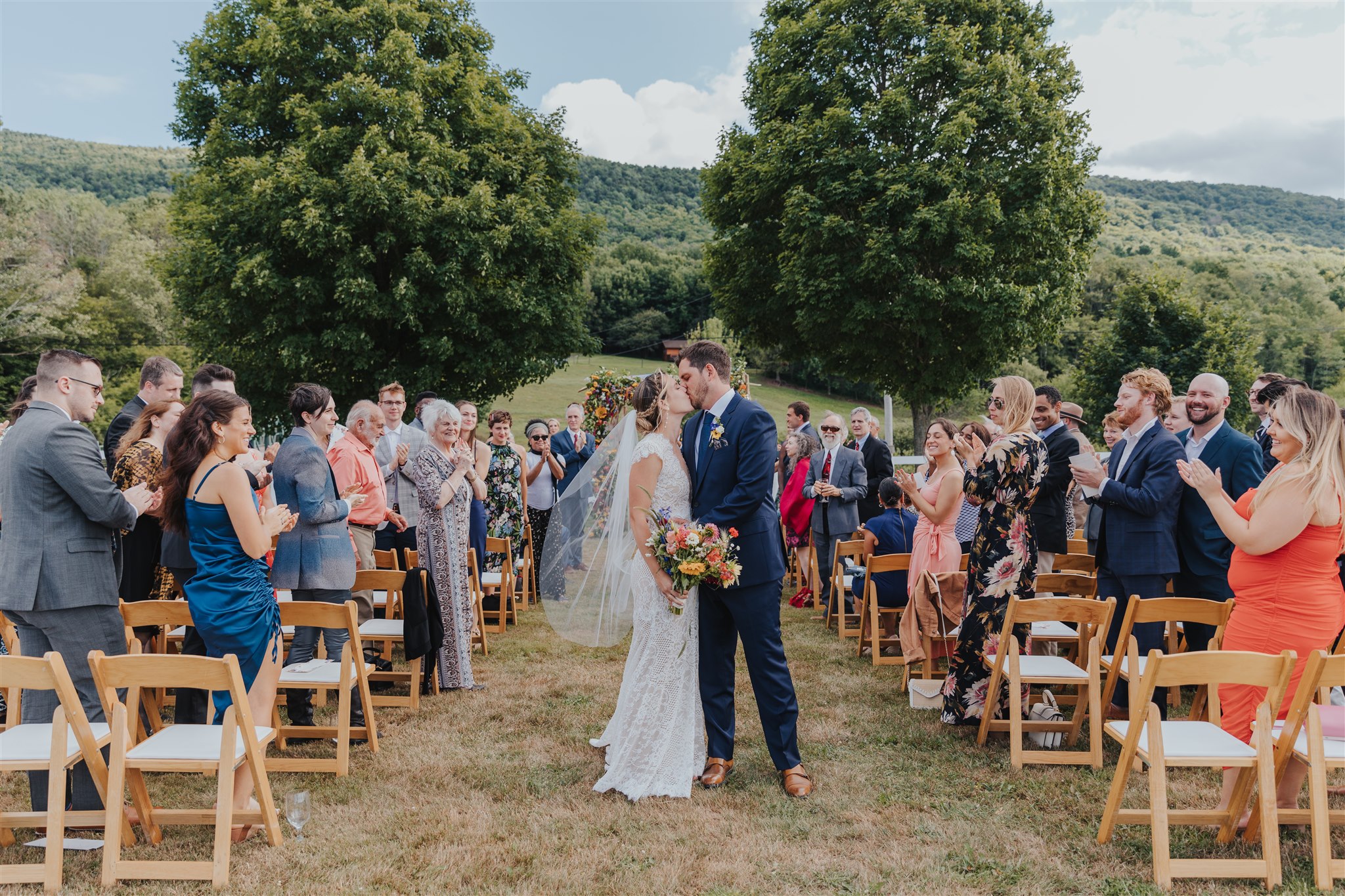 Bride and groom kiss at the end of their ceremony aisle surrounded by cheering guests—showcasing a joyful moment and the cost of home wedding setups.