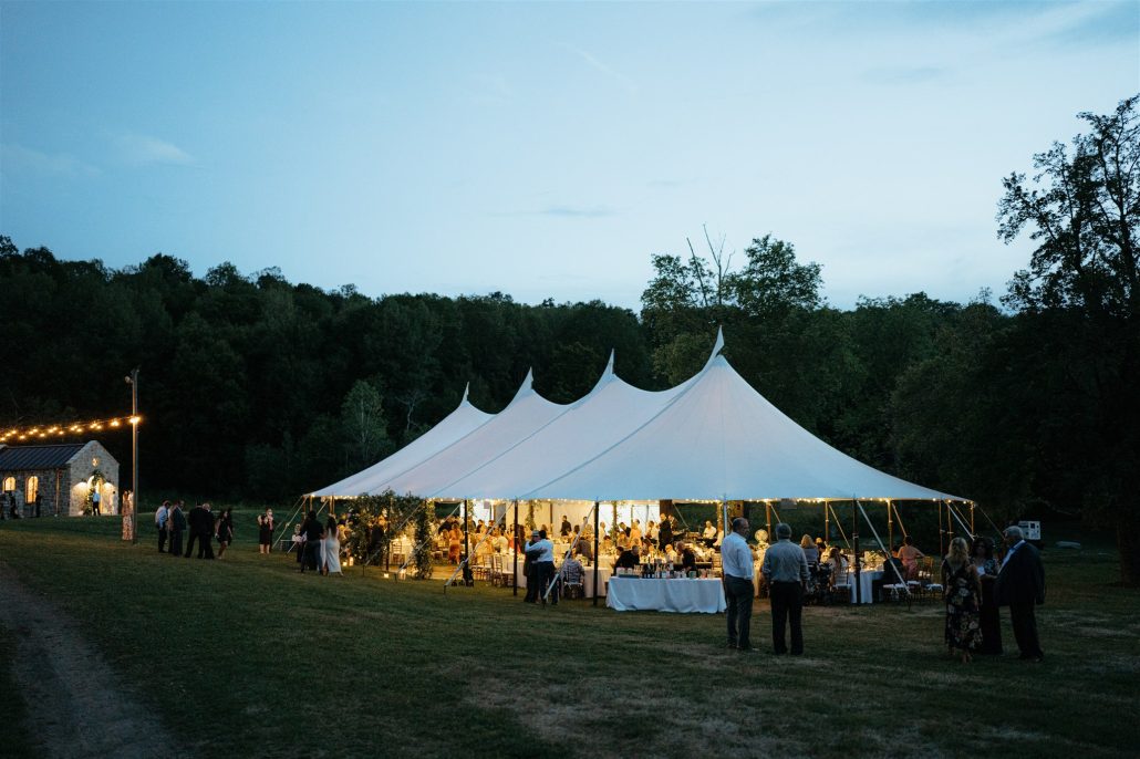 Twilight view of a glowing sailcloth tent in the countryside—capturing ambiance and lighting that add to the cost of home wedding celebrations.