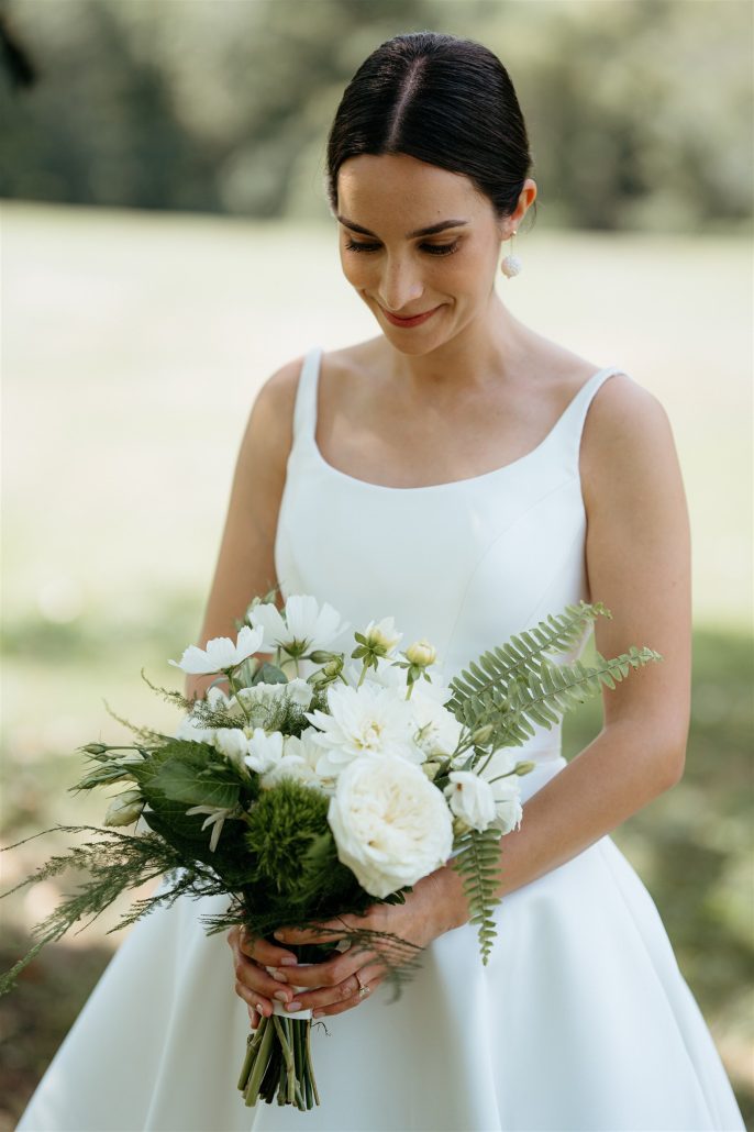 Bride holding a white bouquet and smiling gently before the ceremony—simple, refined bridal styling not always reflected in cost of home wedding estimates.