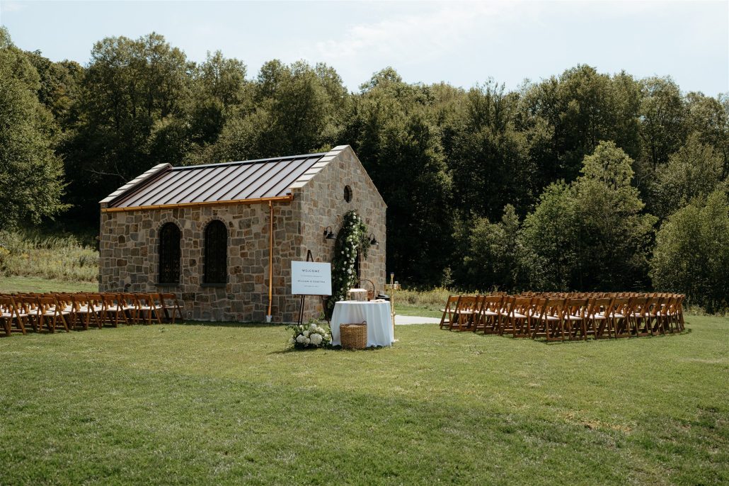 Outdoor ceremony setup in front of a charming stone chapel with guest seating and welcome signage—part of the logistical planning in the cost of home wedding.