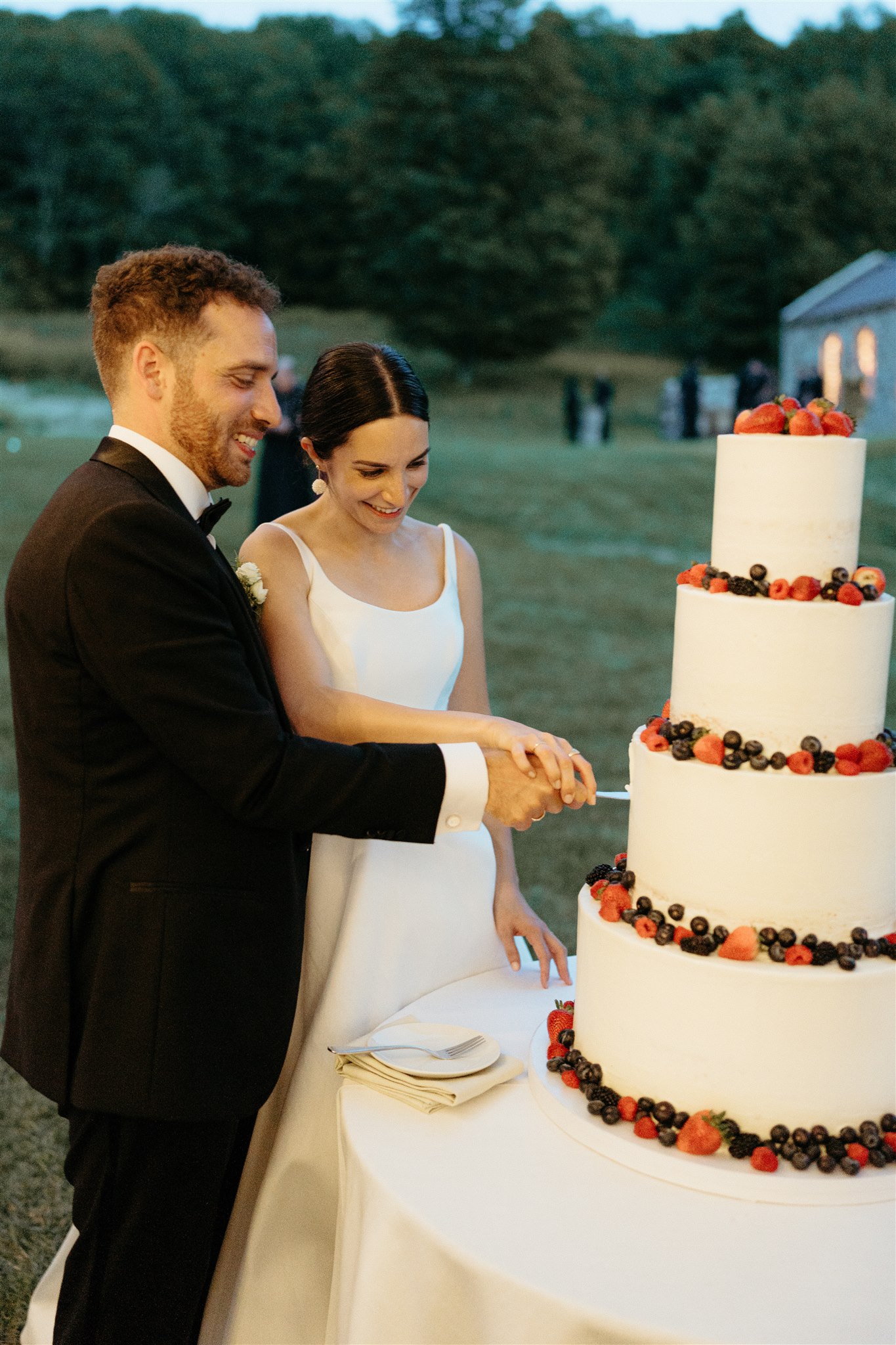 Bride and groom cutting their wedding cake beneath a tented outdoor reception—an elegant moment that reflects the personalized experience and cost of home wedding celebrations.