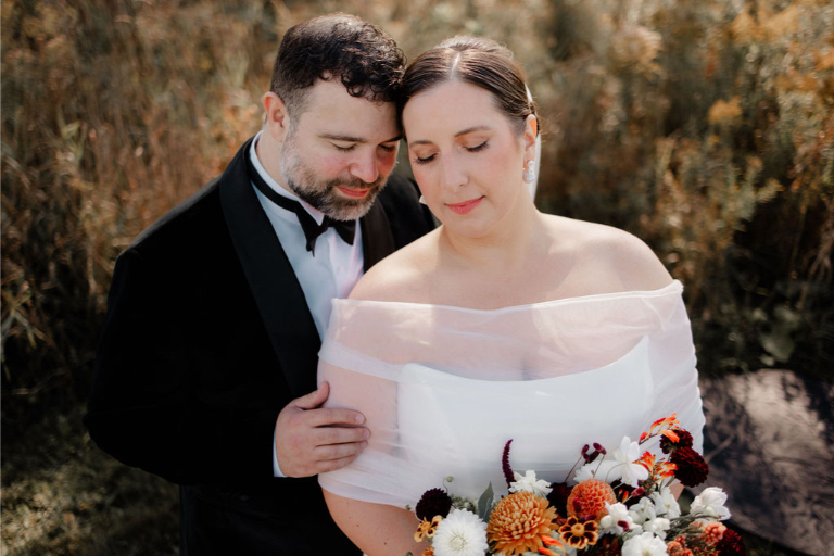 Bride and groom sharing a quiet moment in a wildflower field, holding a fall-inspired bouquet