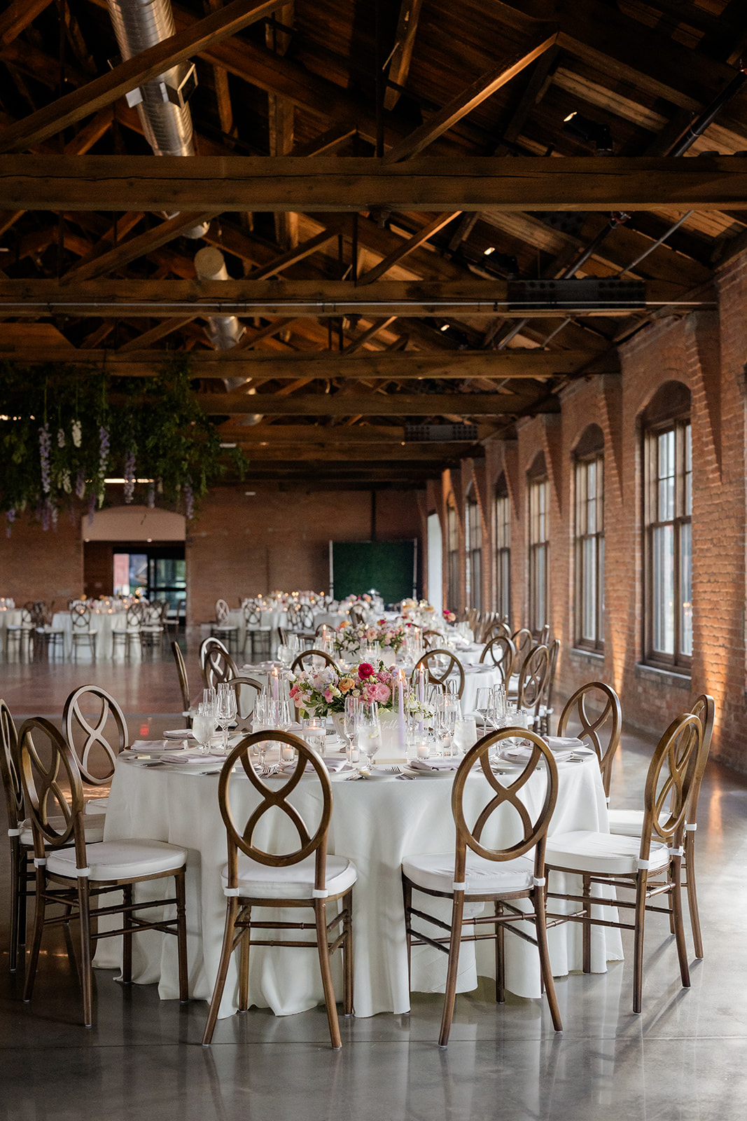 Elegant reception layout with round tables and floral centerpieces beneath exposed wooden beams in a refined event space.