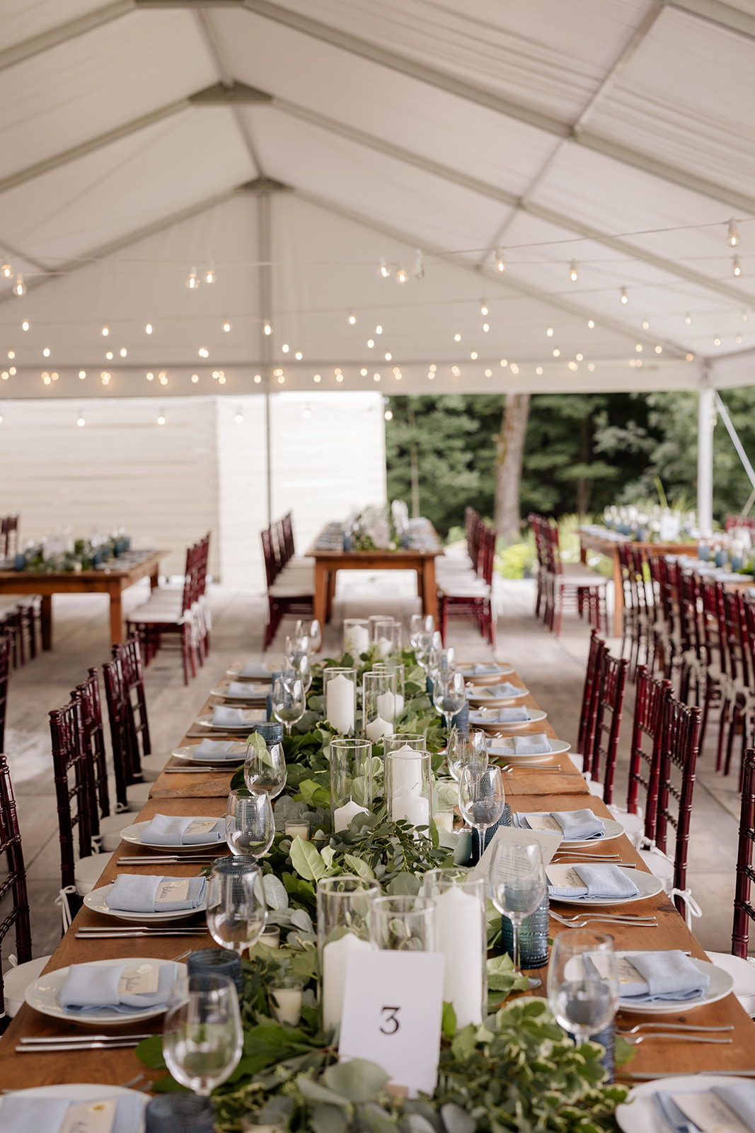Tented outdoor reception with greenery runners, white candles, and soft string lighting—an example of wedding planner vs venue coordinator logistics.