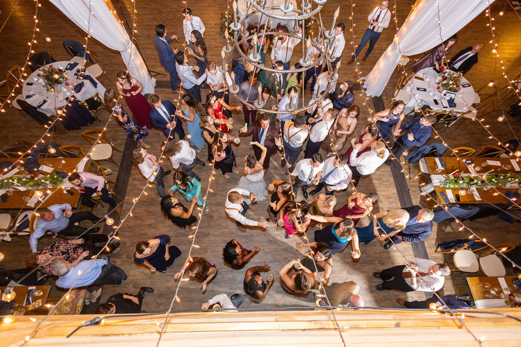 Guests dancing beneath romantic string lights at a rustic wedding reception, capturing joyful energy as part of the best wedding media coverage.