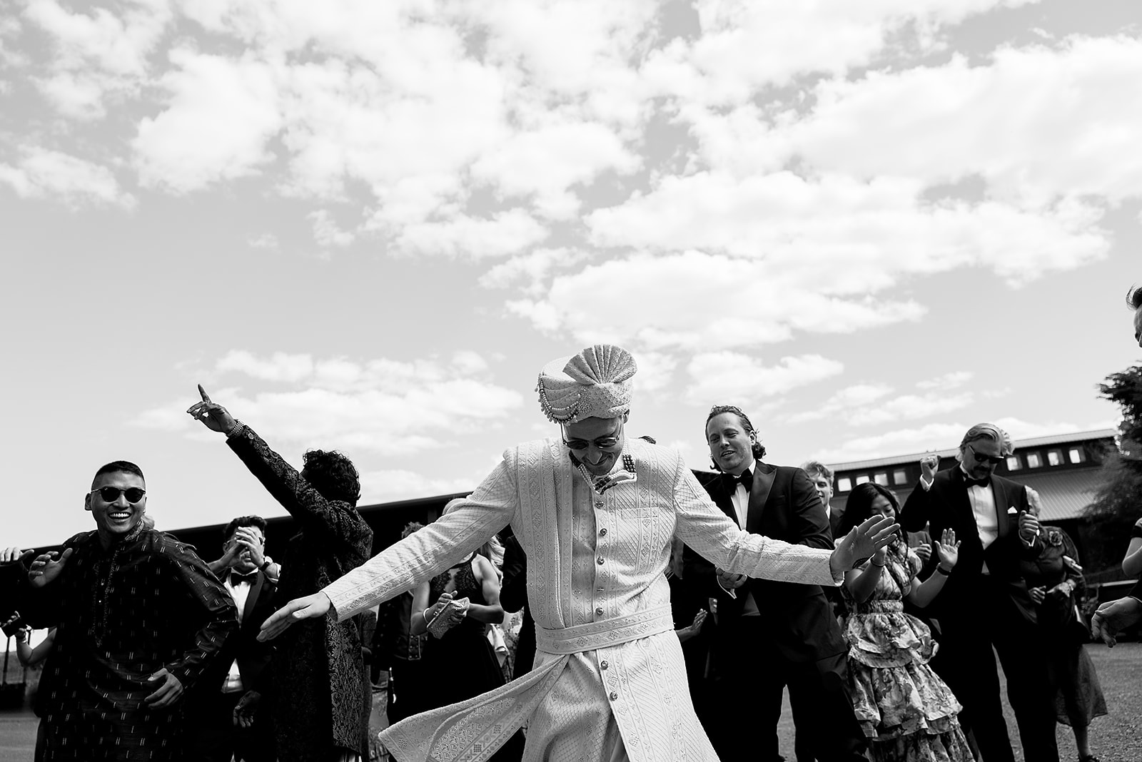 Groom dancing joyfully with guests in a candid black-and-white moment from the baraat.