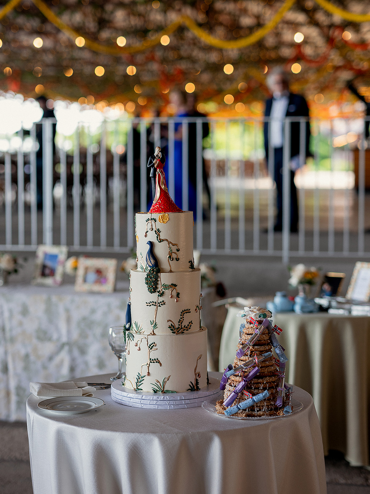 Ornate three-tiered wedding cake with hand-painted florals and a custom bride-and-groom topper, alongside a traditional Scandinavian kransekake tower.