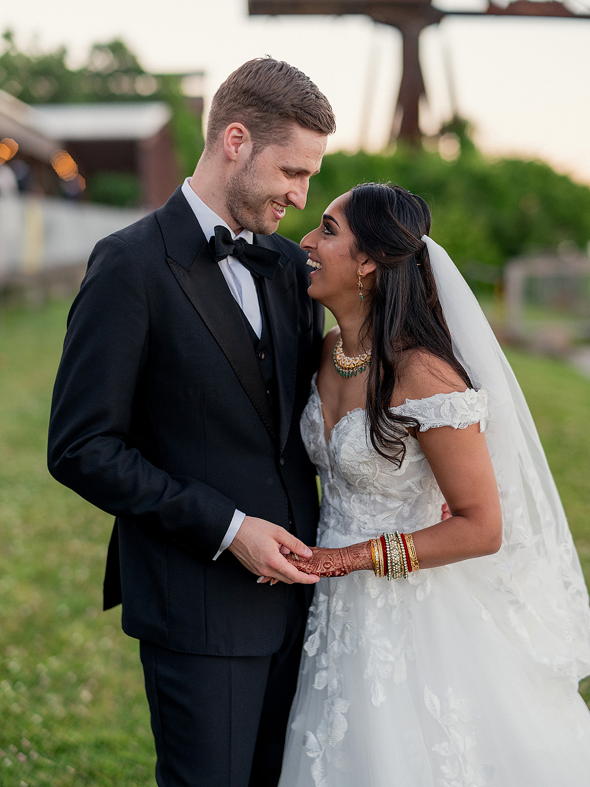 Bride and groom share an intimate moment outdoors at Hutton Brickyards, the bride in an off-shoulder lace gown and the groom in a classic black tuxedo.