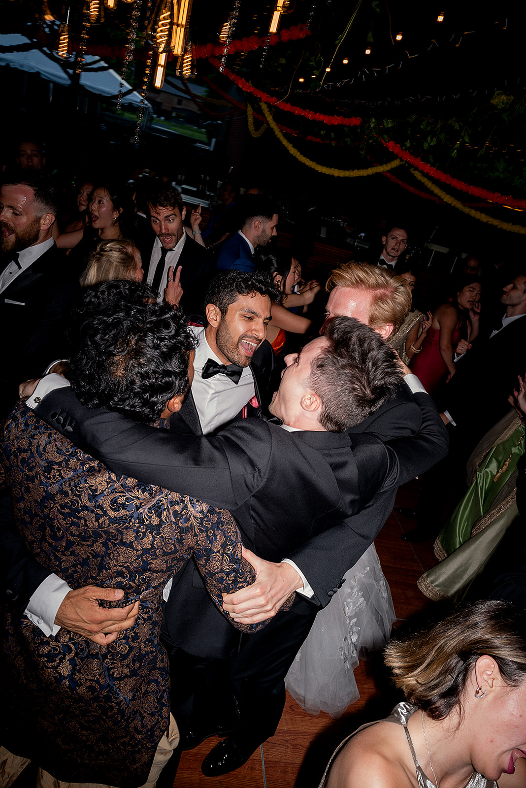 Group of groomsmen laughing and embracing during a lively moment on the wedding reception dance floor.