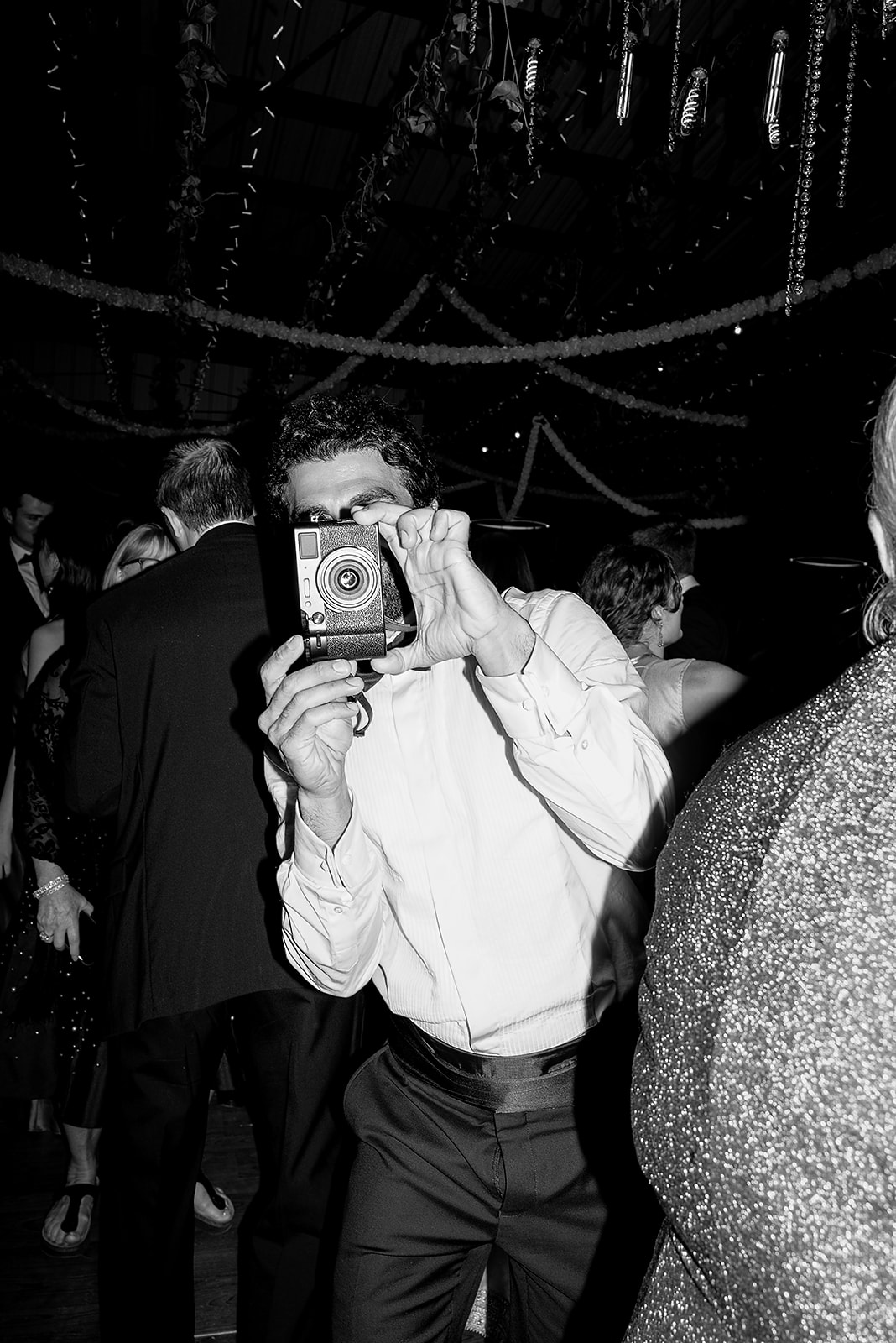 Wedding guest snapping a photo with a vintage film camera amid a festive reception atmosphere.