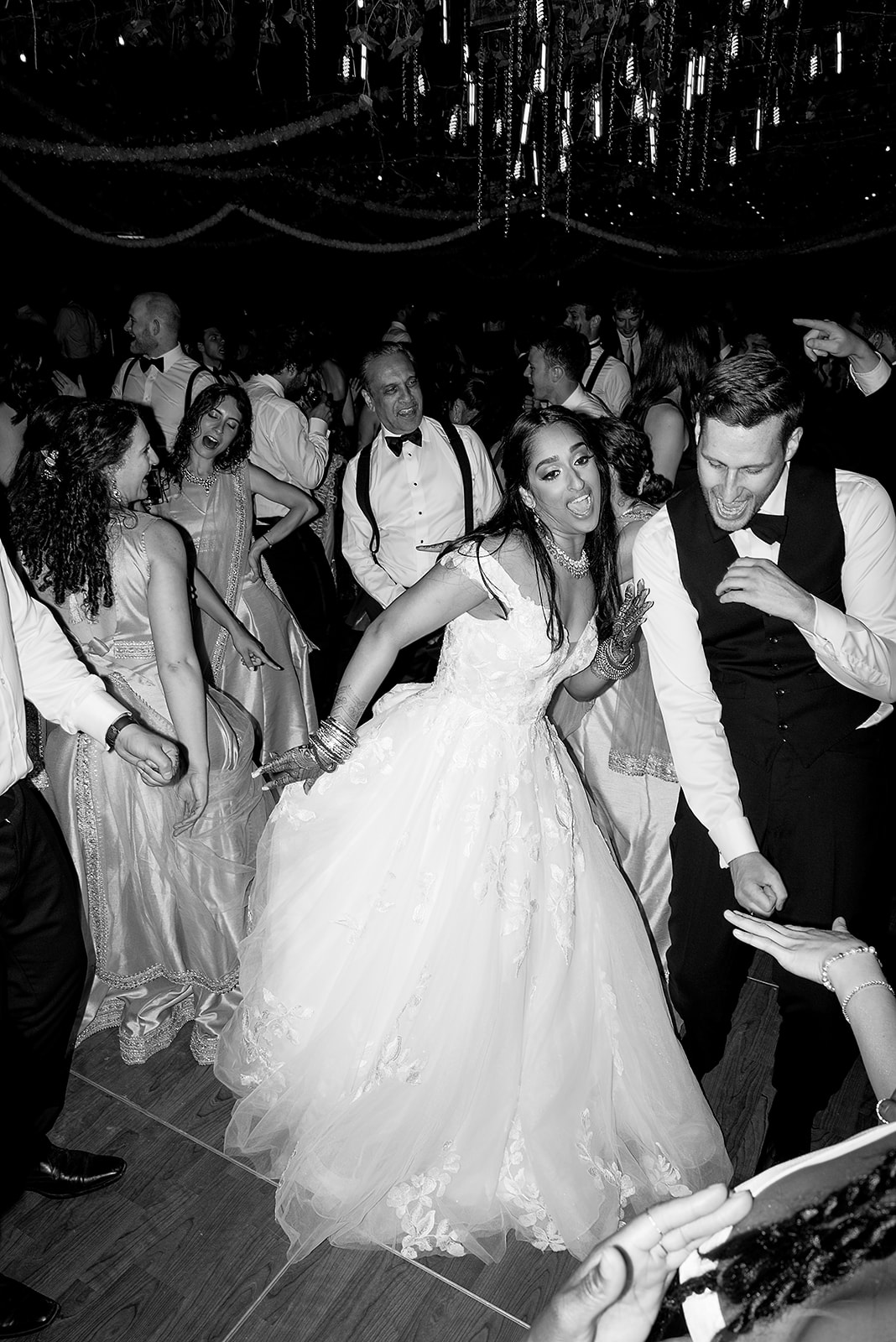 Bride and groom dancing joyfully during their reception, surrounded by guests on the packed dance floor.
