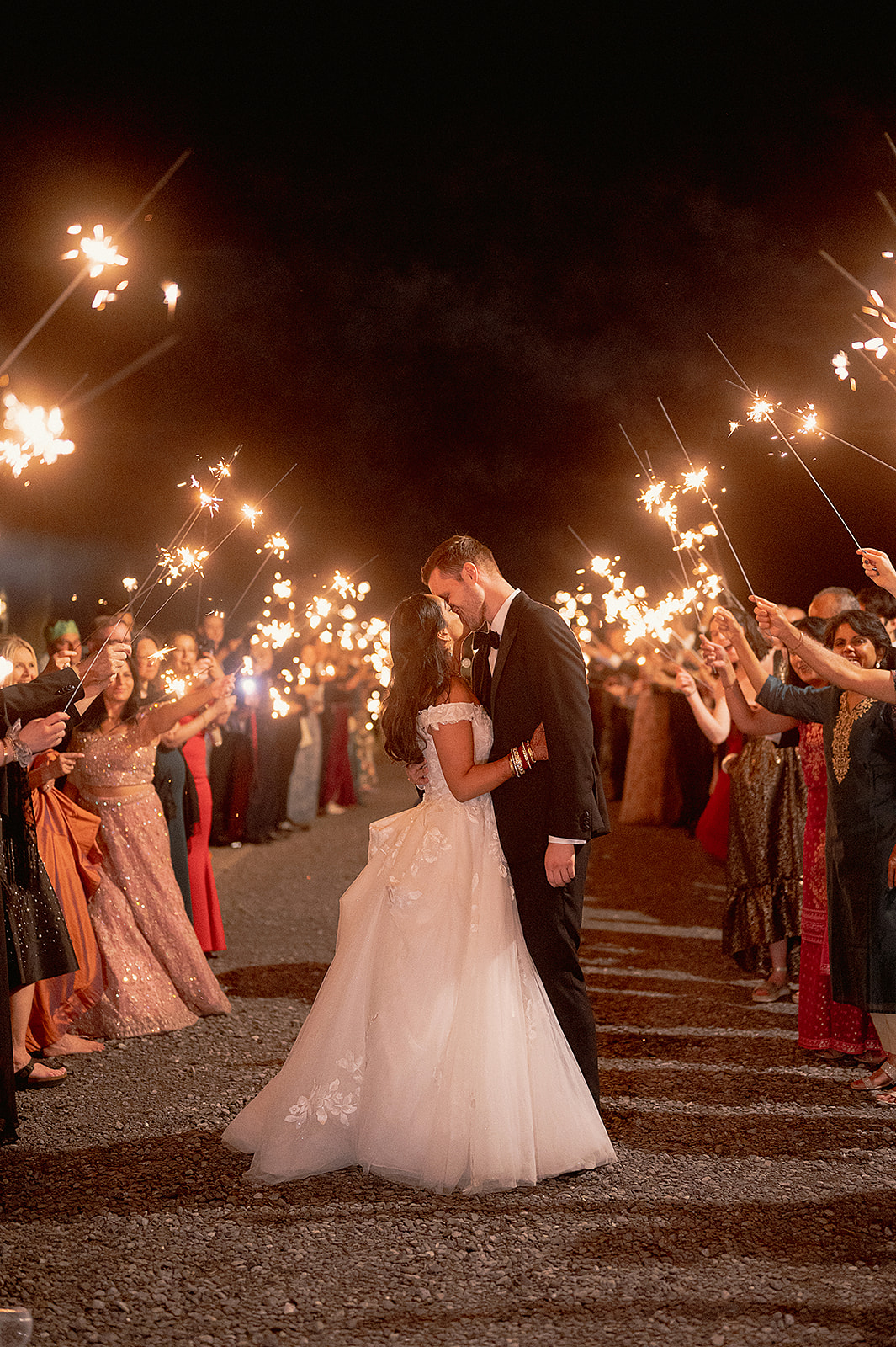 Bride and groom share a romantic kiss beneath a canopy of sparklers during their wedding night send-off.