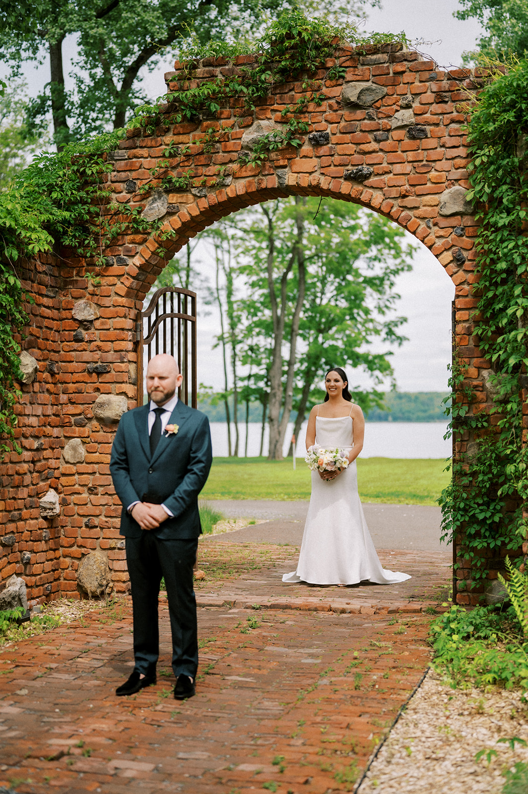 Bride approaches groom for a first look beneath a vine-covered brick arch at a Hudson Valley wedding venue with accommodations.
