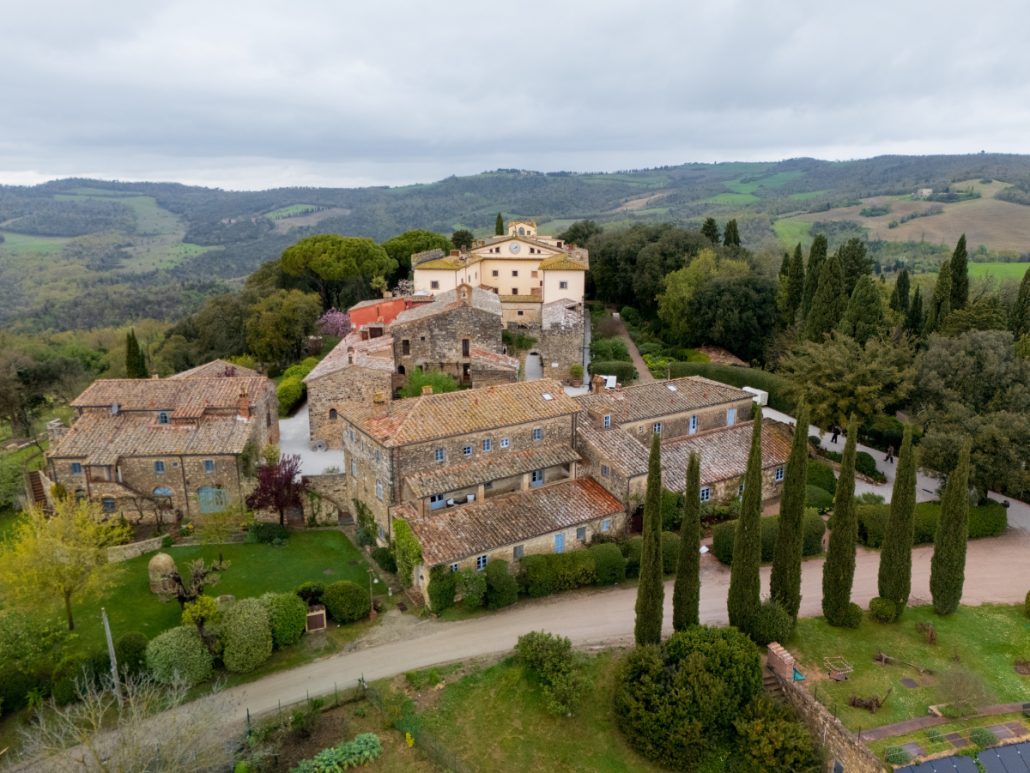 Drone view of historic Tuscan estate with terracotta rooftops, cypress trees, and green hills ideal for weddings.
