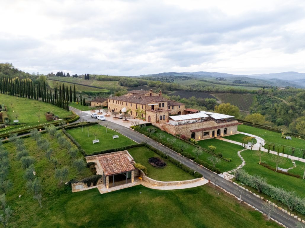 Aerial view of a luxury wedding venue in Tuscany with stone villa, manicured lawns, and rolling vineyard hills in the background.