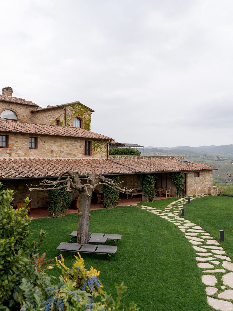 Stone villa with terracotta roof, green lawn, and shaded garden seating at a charming Tuscan wedding venue.