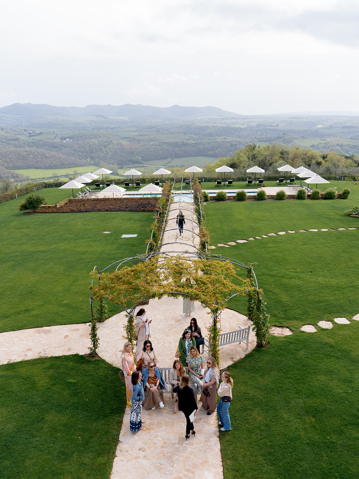 Guests gathering under a flower-covered arch in manicured gardens with sweeping Tuscan hills at Fontanelle Estate Tuscany wedding venue.
