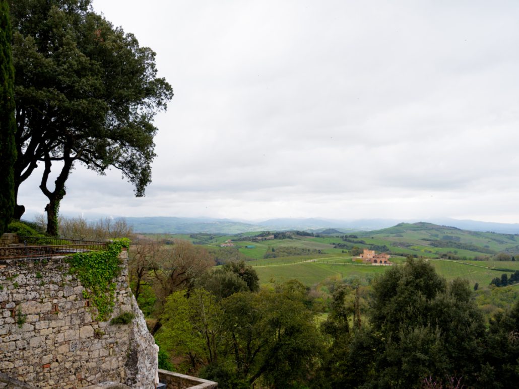 Panoramic view of rolling hills and vineyards in Tuscany with a rustic stone villa, a serene setting for Italian wedding venues.