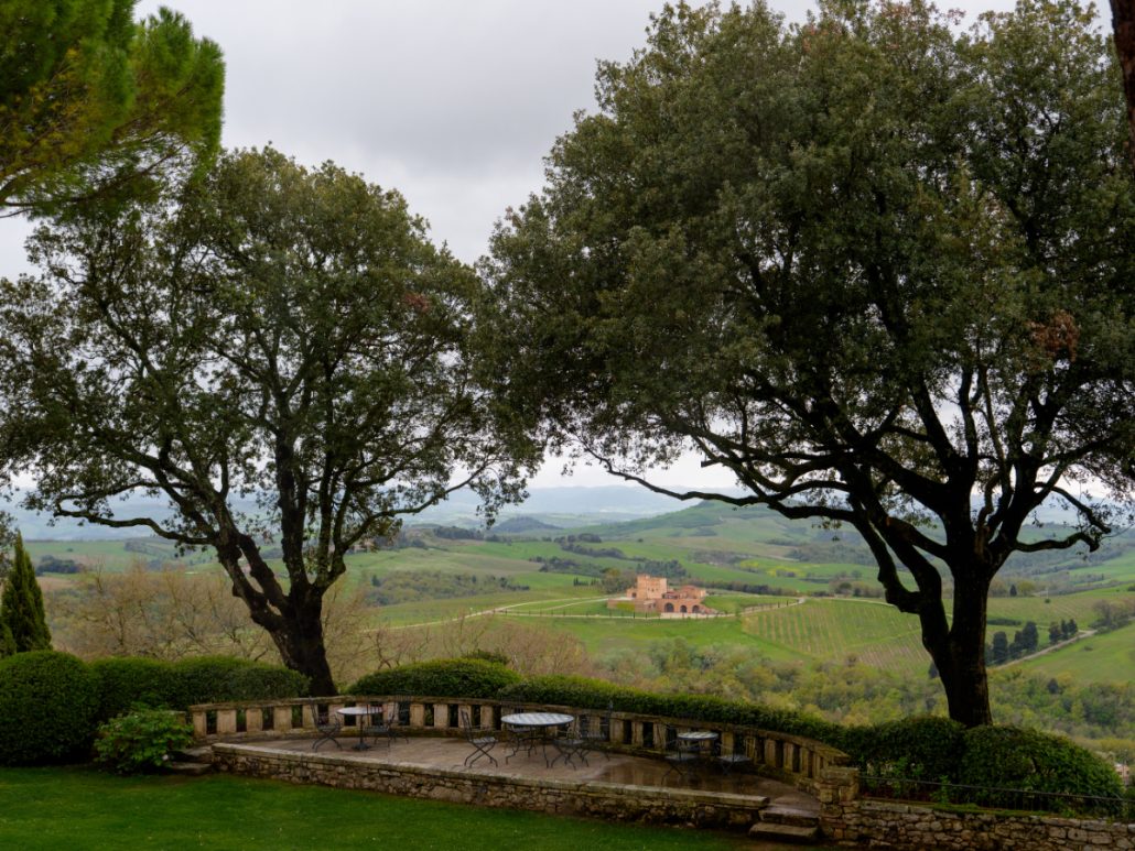 Panoramic view of Tuscan vineyards and villas framed by oak trees from Borgo Pignano, a serene wedding venue in Tuscany.