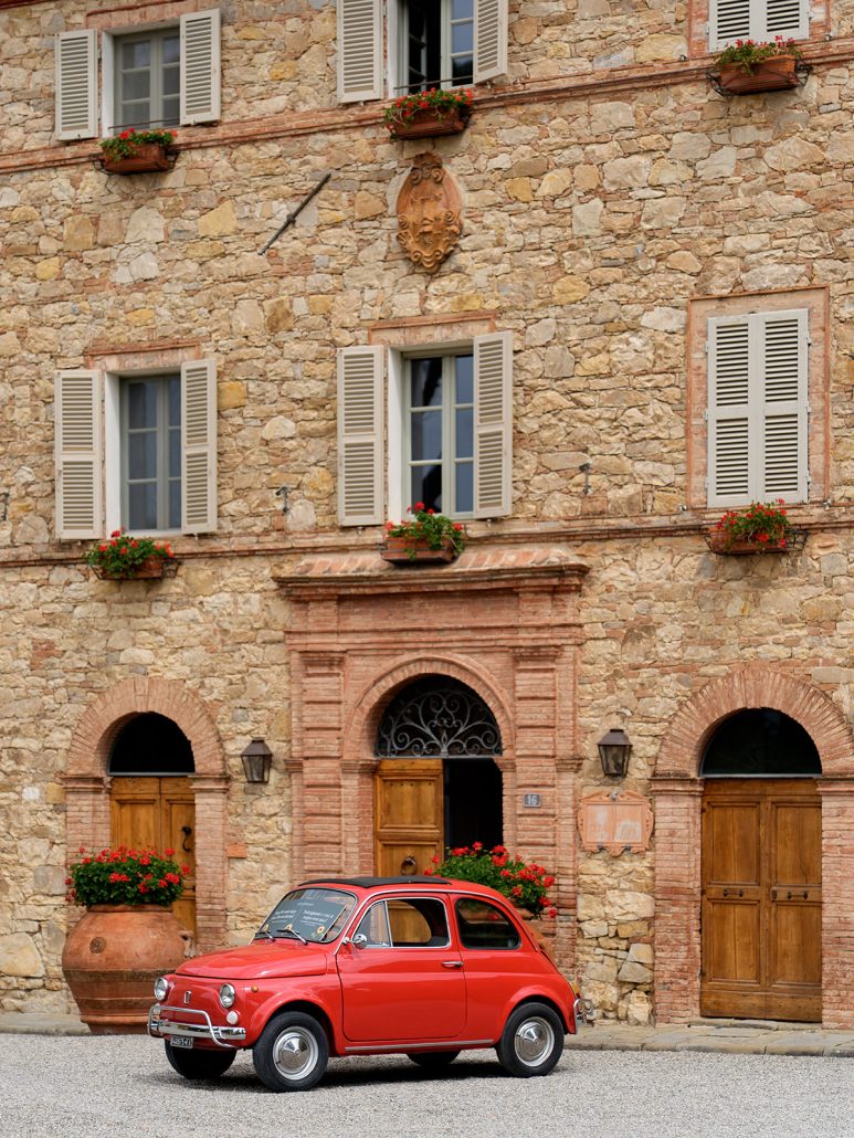 Classic red Fiat 500 parked in front of Borgo San Felice Resort, a rustic Tuscan wedding venue with stone walls and shuttered windows.