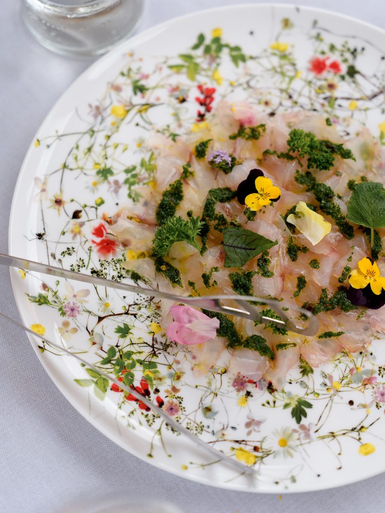 Elegant dish served at Borgo San Felice Resort, Tuscany — thinly sliced fish with herbs and edible flowers on a floral plate.