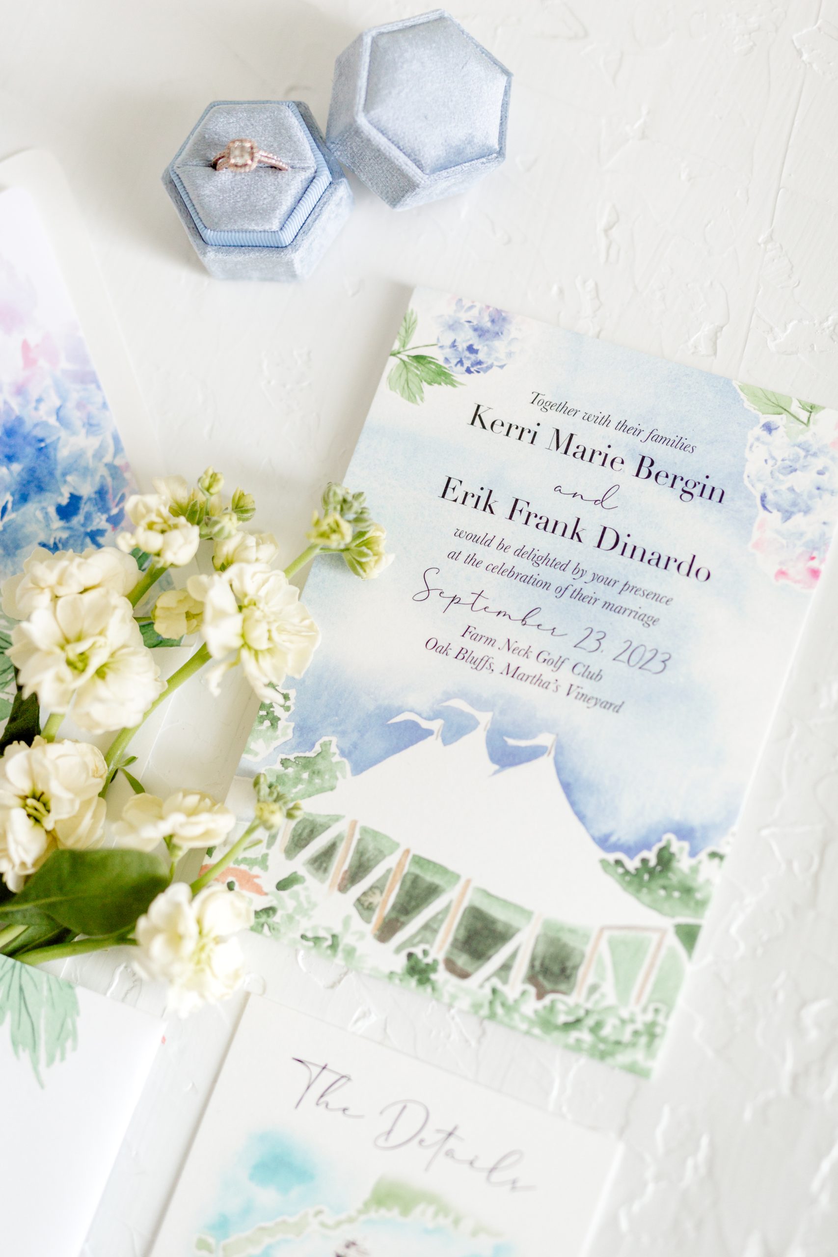 Elegant tented wedding invitation with soft floral artwork, paired with a light blue velvet ring box.
