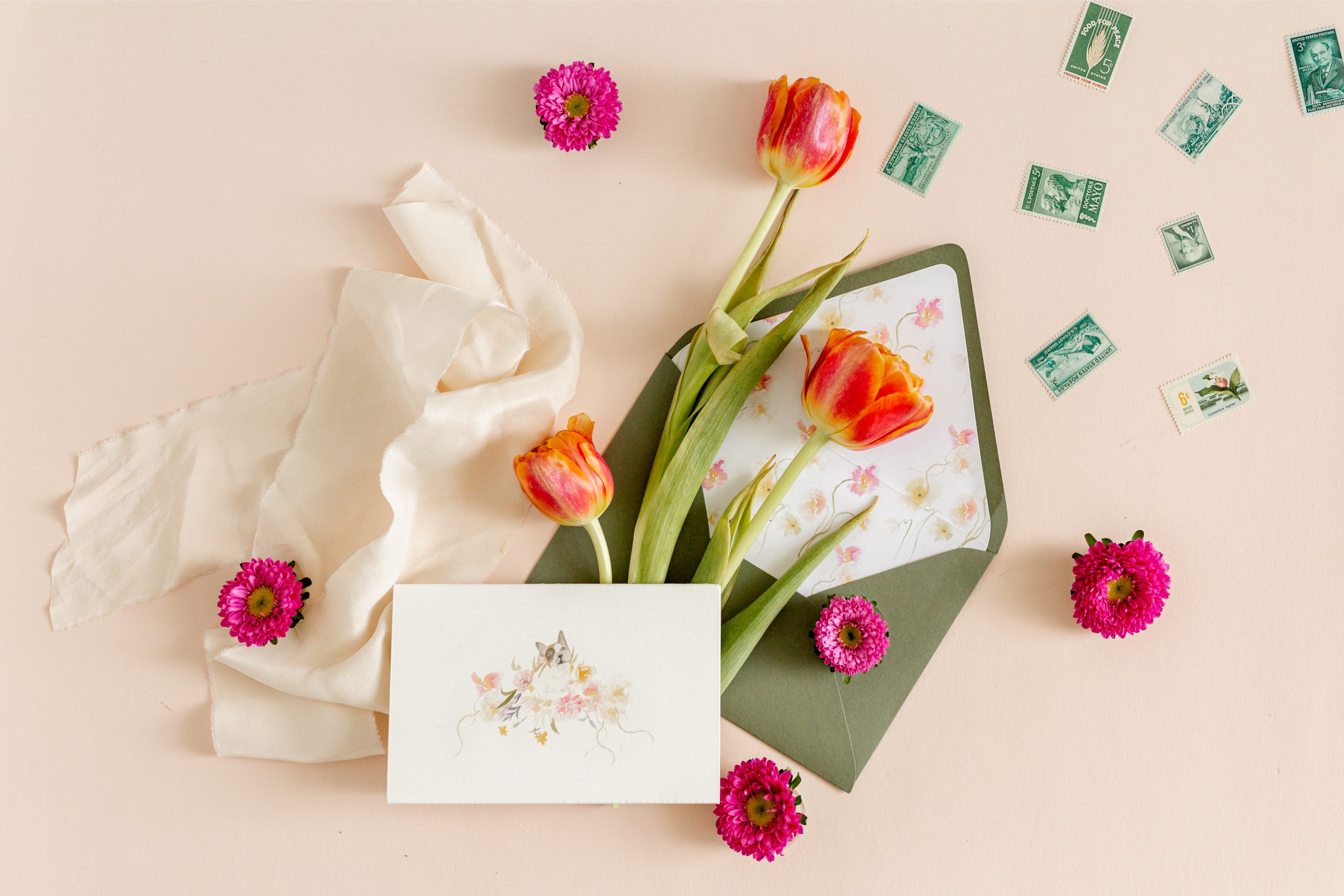 A romantic wedding envelope lined with floral art and surrounded by fresh tulips and vintage stamps.
