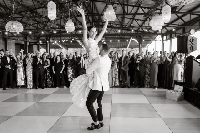 Couple sharing their first dance surrounded by guests at their elegant summer wedding reception.