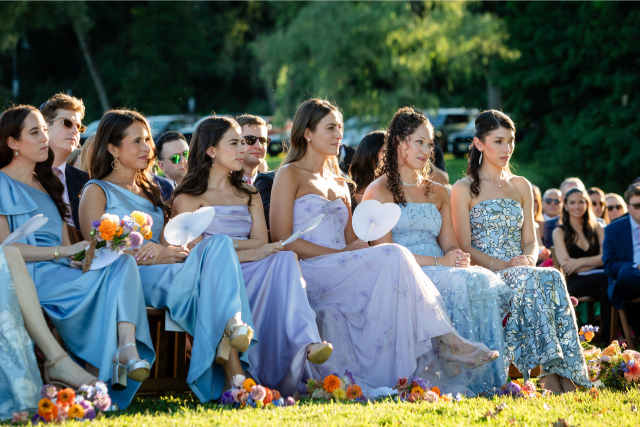Bridesmaids fanning themselves with white paper fans during the ceremony