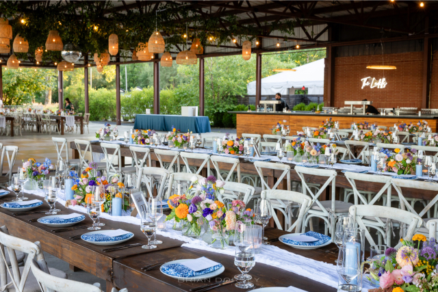 Reception tables with colorful floral arrangements, blue napkins, and open-air views of the Hudson River at Hutton Brickyards.