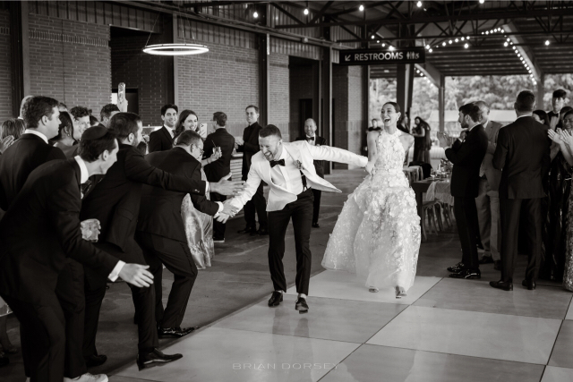 Black-and-white photo of groom high-fiving guests as the couple enters the dance floor.