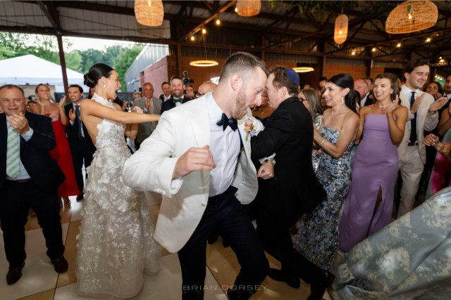 Guests dancing joyfully on the floor under twinkling lights during a lively summer Hudson River wedding at Hutton Brickyards.