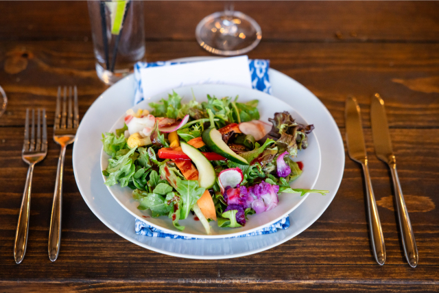 A fresh and colorful summer salad served on a wooden table setting with blue napkin and gold flatware.