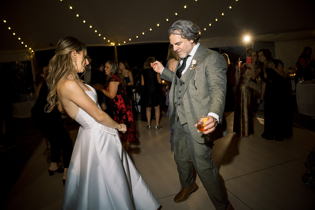 Couple dancing joyfully under string lights on the reception dance floor.