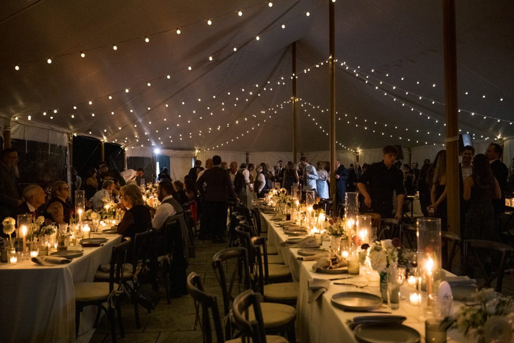 Guests gathered beneath a warmly lit tent during a Scribner’s Catskill Lodge wedding reception at night.