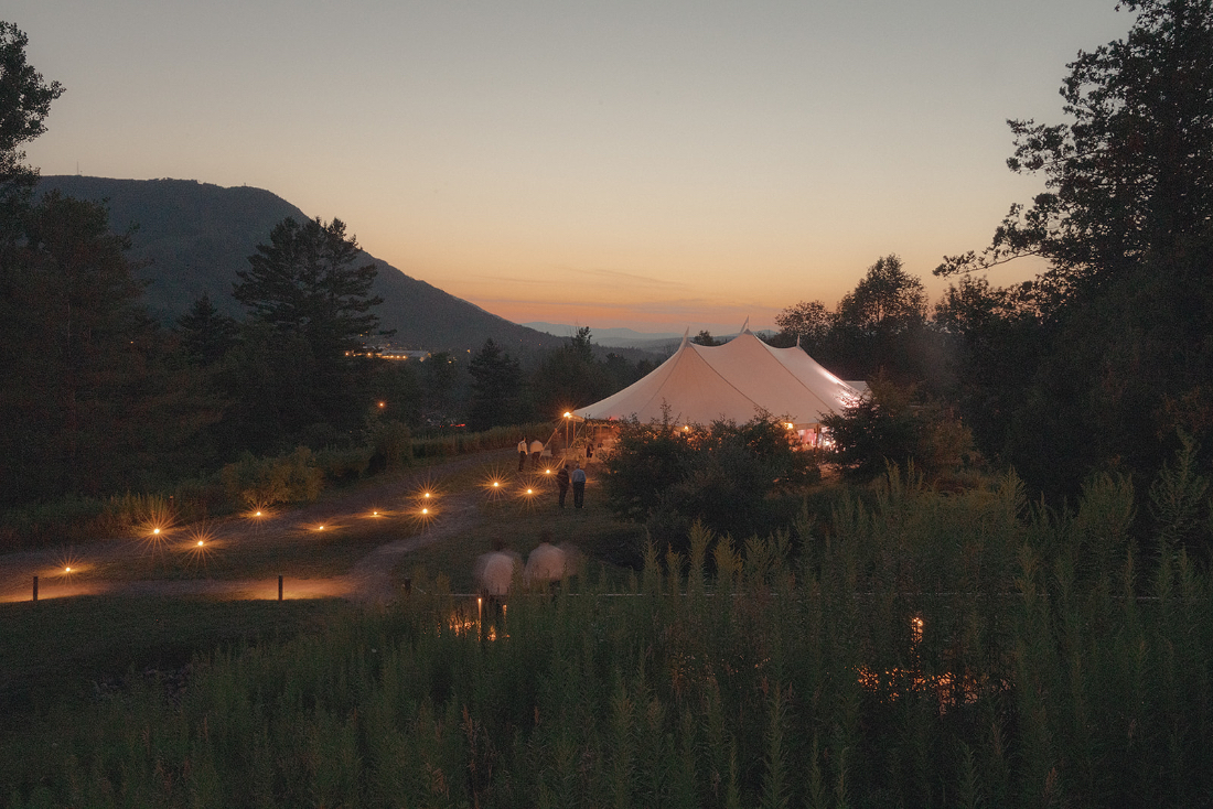 Wide evening view of the lit tent and surrounding landscape at a Scribner’s Catskill Lodge wedding.