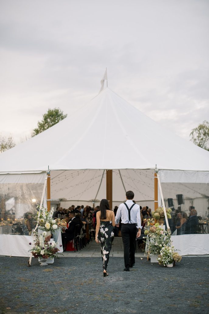 Guests walking into the warmly lit reception tent decorated with seasonal florals.