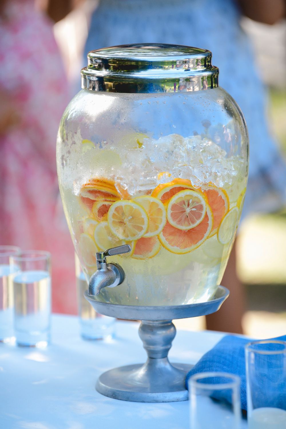 A glass beverage dispenser filled with citrus slices and ice at a buttermilk falls inn wedding outdoor refreshment table.