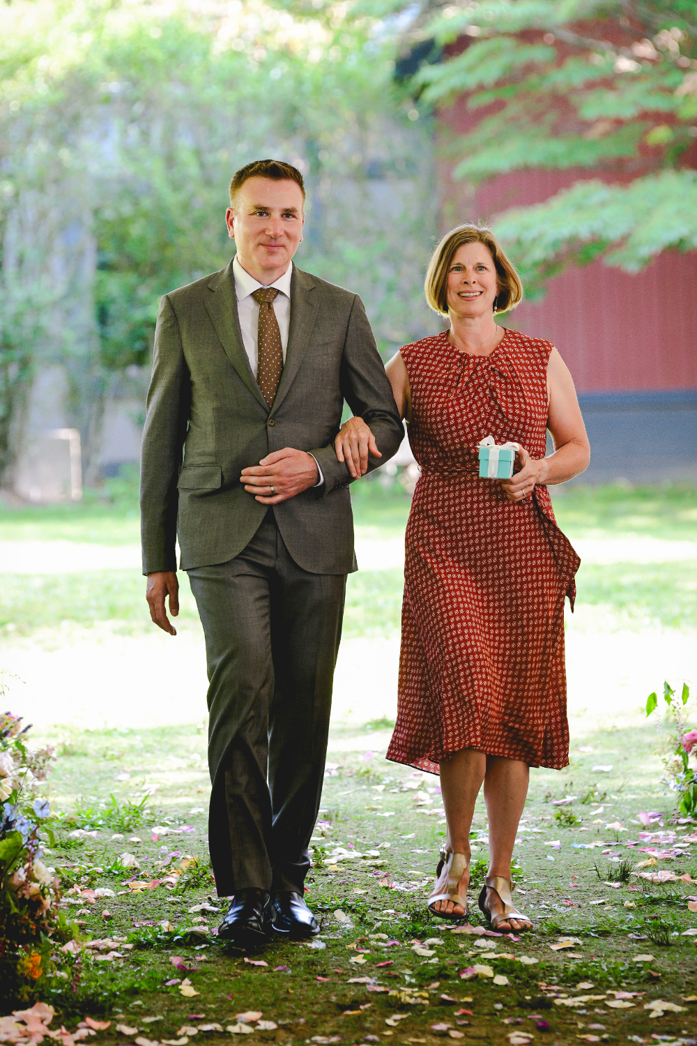 Two guests walk down the petal-covered aisle carrying a small gift box at a buttermilk falls inn wedding.