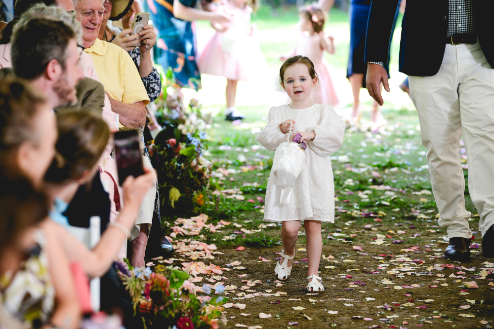Flower girl walking down a petal-lined aisle during a Buttermilk Falls Inn wedding, holding a small basket and surrounded by smiling guests.
