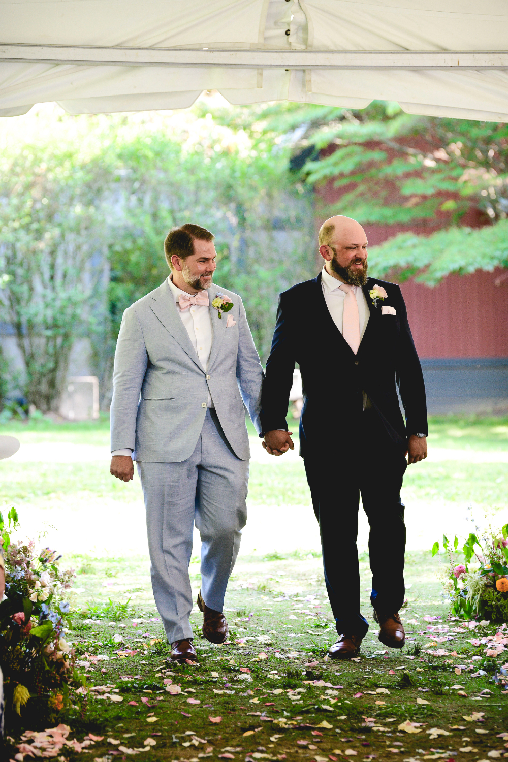 Grooms walking together through a petal-covered aisle at their Buttermilk Falls Inn wedding, surrounded by natural greenery.